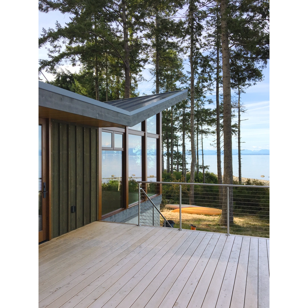 A beach house with green board and batten siding, large windows and a large yellow cedar deck facing the ocean.