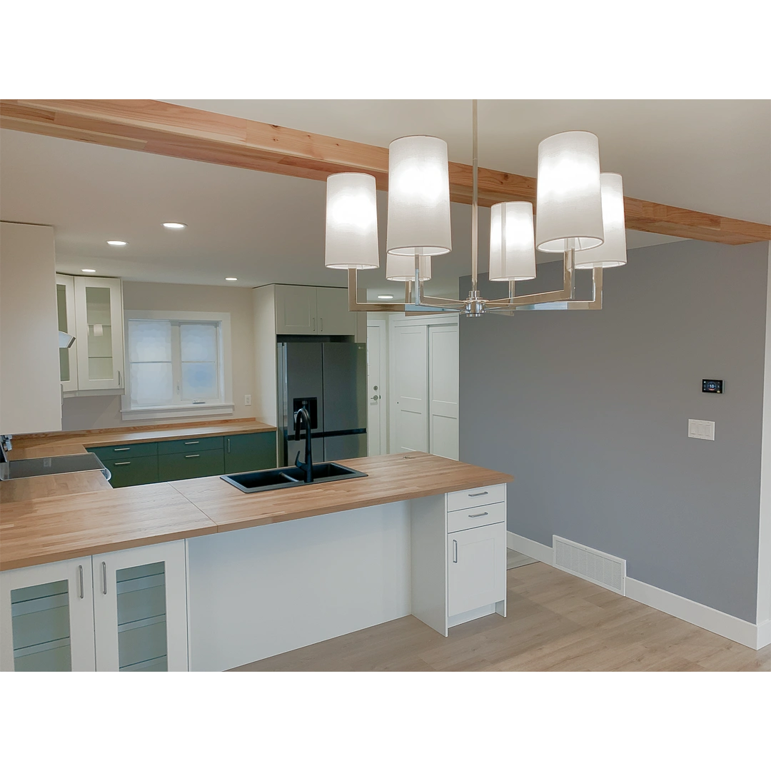 A U-shaped kitchen with grey-green lower cabinets and white upper cabinets, a lavender accent wall and a beam wrapped in laminated red cedar.