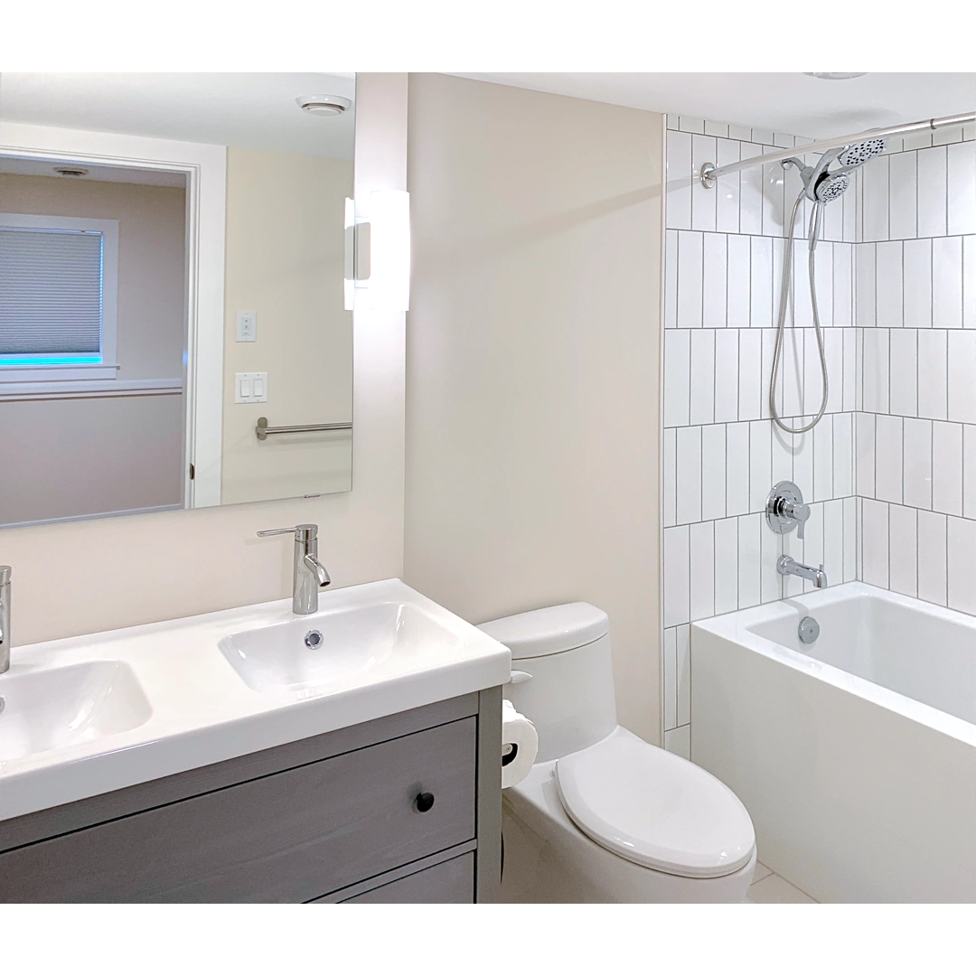 A modern bathroom with double sink, toilet, and a shower tiled with vertical white subway tile.